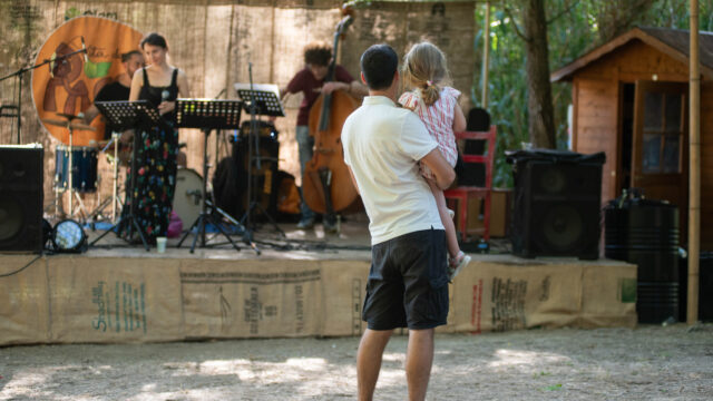Padre con una bambina in braccio che ascoltano un concerto all’aperto in un bioparco.