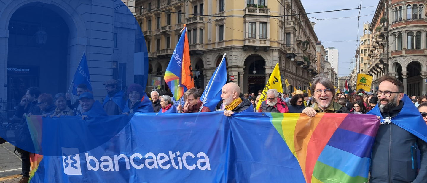 Corteo in piazza a Milano con partecipanti che reggono uno striscione di Banca Etica e bandiere.