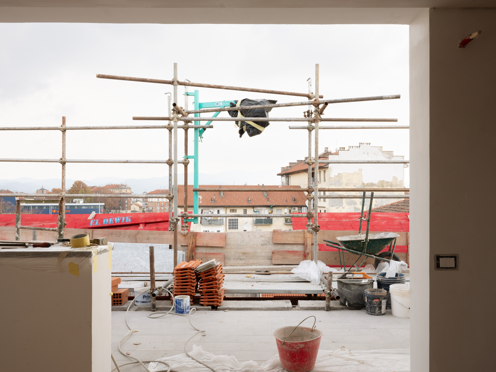 Cantiere edile in corso: impalcatura, materiali da costruzione e, sullo sfondo, i tetti di un quartiere urbano